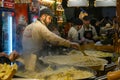 A staff of a Christmas market stands stirring the gigantic hot pan filled with pasta and cheese