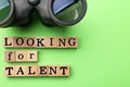 Staff recruitment concept. Phrase Looking For talent made of wooden cubes and binoculars on green background, flat lay. Space for