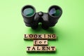 Staff recruitment concept. Phrase Looking For Talent made of wooden cubes and binoculars on light green background, above view