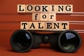 Staff recruitment concept. Phrase Looking For Talent made of wooden cubes and binoculars on orange background