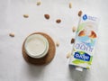 Staging of a brick of Alpro vegetable milk next to a glass of almond milk with almonds. On white light background.