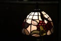 Stained glass lampshade glowing in darkness. Table lamp closeup on black background. Mosaic made from white and colorful glass Royalty Free Stock Photo