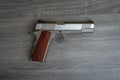 Stainless hand gun with brown hand grip is on the wooden floor