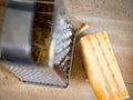 Stainless steel cheese grater on a wooden cutting board, alongside a cube of white cheddar cheese Royalty Free Stock Photo