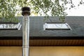 Stainless steel chimney flue on the tile covered roof with windows at country cottage Royalty Free Stock Photo