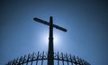 Stainless steel cross and fence on blue sky and sun light background. Crucifix of Jesus Christ. God light and forgiveness concept.
