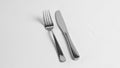 A stainless steel fork and knife are placed side by side on a white Royalty Free Stock Photo