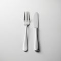 A stainless steel fork and knife rest side by side on a flat white surface. The fork, with four Royalty Free Stock Photo