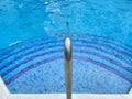 Stainless steel handrail descending in clear pool water with steps Royalty Free Stock Photo