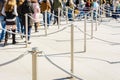 Tourists standing in line between stainless steel queue poles linked by grey ropes under a bright sunshine