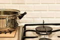 Stainless steel pot stands next to gas burner against white brick kitchen wall. Kitchen interior with gas stove and utensils. Royalty Free Stock Photo