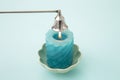 Stainless steel put out candle flame wick long handle candle snuffer bell with lit blue candle on blue studio background.