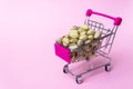 Stainless steel small miniature toy shopping trolley with pistachio nuts inside on pink background. Shopping, mall, business