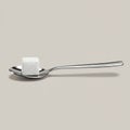 A stainless steel spoon holds a single white sugar cube. The cube is composed of tiny Royalty Free Stock Photo
