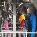 Stainless steel spoons and forks and children`s multi-colored plastic dishes in a cutlery basket inside the dishwasher Royalty Free Stock Photo