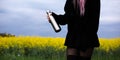 Stainless thermos bottle in hand of young girl dressed in black with pink hair, on background of rapeseed field.