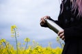 Stainless thermos bottle in hand of young girl dressed in black with pink hair, on background of rapeseed field.