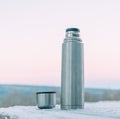 Stainless thermos and cup on snowy background.