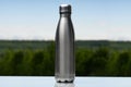 Stainless thermos, water bottle on the sky and forest background.