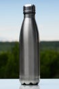 Stainless thermos, water bottle on the sky and forest background. Vertical photo.
