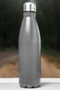 Stainless thermos water bottle on white table, outdoor. Black color.