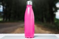 Stainless thermos water bottle on white table, outdoor. Pink color.