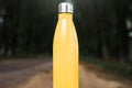 Stainless thermos water bottle on white table, outdoor. Yellow color.