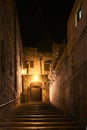 The staircase is illuminated with a yellowish color. Dark nightly narrow streets of the old city,