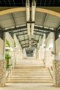 Staircase along exterior hallway corridor with high ceiling, lights and fixtures above and along stone wall columns