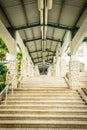 Staircase along exterior hallway corridor with high ceiling, lights and fixtures above and along stone wall columns.