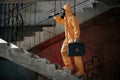 On stairs with flashlight and case. Man dressed in chemical protection suit in the ruins of the post apocalyptic building