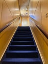 A stairway on a cruise ship with blue carpet and cream colored walls leading up to the luxury Retreat