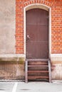 Stairway to old closed rusty metal door in red brick wall. Urban and industrial image. Vertical with copy space.