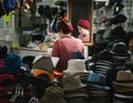 Stall in an underground mall. Female seller is reflected on a mirror. She is framed by the hats displayed at her shop. Picture