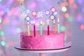 Stand with delicious birthday cake and burning candles against blurred lights Royalty Free Stock Photo