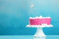 Stand with delicious birthday cake and sparkler on table against color background Royalty Free Stock Photo