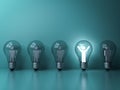 One glowing light man standing with arms wide open in light bulb among other dim people on dark green pastel background Royalty Free Stock Photo