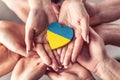 We stand with Ukraine symbol as numerous hands hold one another in unity with a wooden heart painted in Ukrainian flag colors on