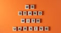 We stand with Ukraine word phrase in wooden letters. Motivation and slogan. Orange background