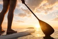 Stand up paddle boarding on quiet sea, legs close-up, sunset