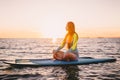 Stand up paddle boarding on a quiet sea with warm sunset colors. Young slim girl is relaxing on ocean