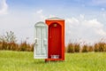 Standalone of red toilet with white door open contrast with green grass and tree in the meadow.