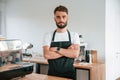 Standing with arms crossed. Cafe worker in white shirt and black apron is indoors Royalty Free Stock Photo