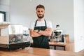 Standing with arms crossed. Cafe worker in white shirt and black apron is indoors Royalty Free Stock Photo