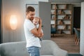 Standing with baby in hands. Father with toddler is at home, taking care of his son