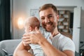 Standing with baby in hands. Father with toddler is at home, taking care of his son