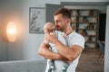 Standing with baby in hands. Father with toddler is at home, taking care of his son