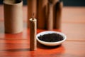 Standing brown firecrackers close to a white bowl with gunpowder, over a wooden table