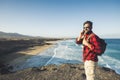 Standing caucasian man calling at the phone on a isolate cliff with ocean waves view - backpacker alternative lifestyle vacation