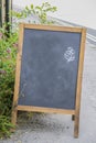 Standing chalkboard sandwich sign sitting outside on rough pavement with a rough flower drawn in corner - room for copy and some